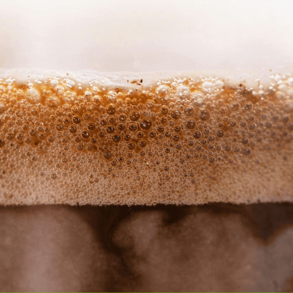 Close up of a layered coffee beverage with dark coffee on the bottom, golden foam above it, and creamy white on top.